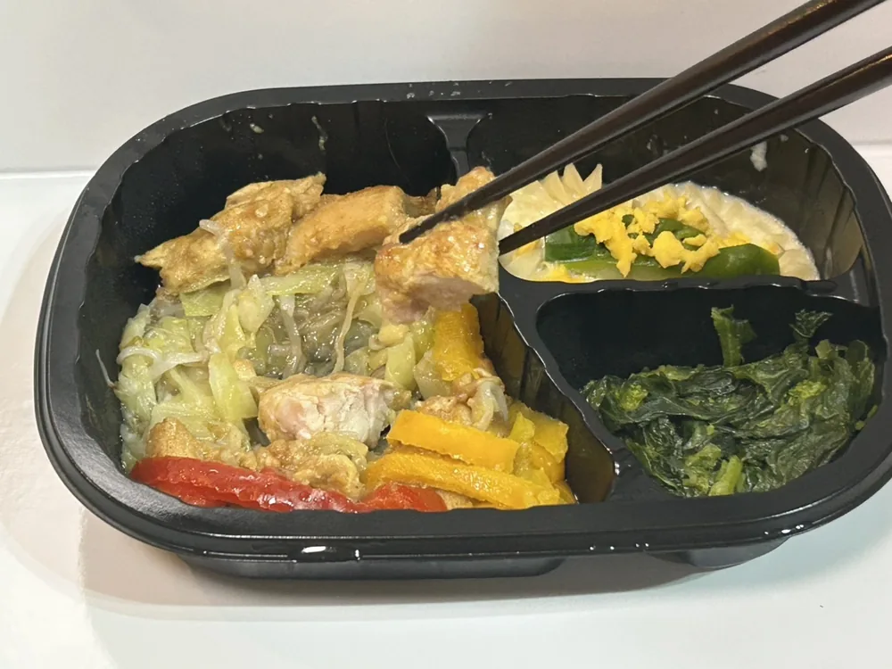 健康直球便 Cタンドリーチキンの主菜を箸で持ち上げたところ。キャベツともやしと一緒に炒められている